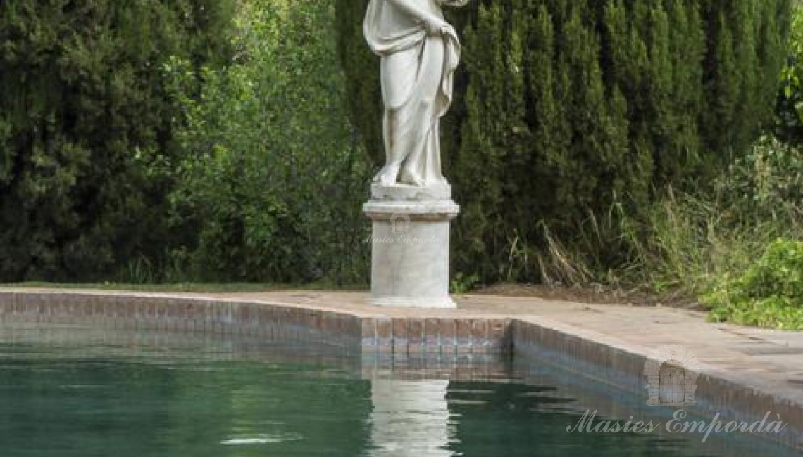 Vista de la piscina rodeada de cipreses con una preciosa estatua estilo romano