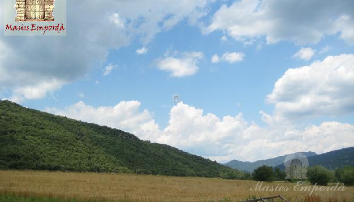 Vista de los campos que rodean la propiedad y colinas colindantes como fondo el azul del cielo moteados de nubes blancas  