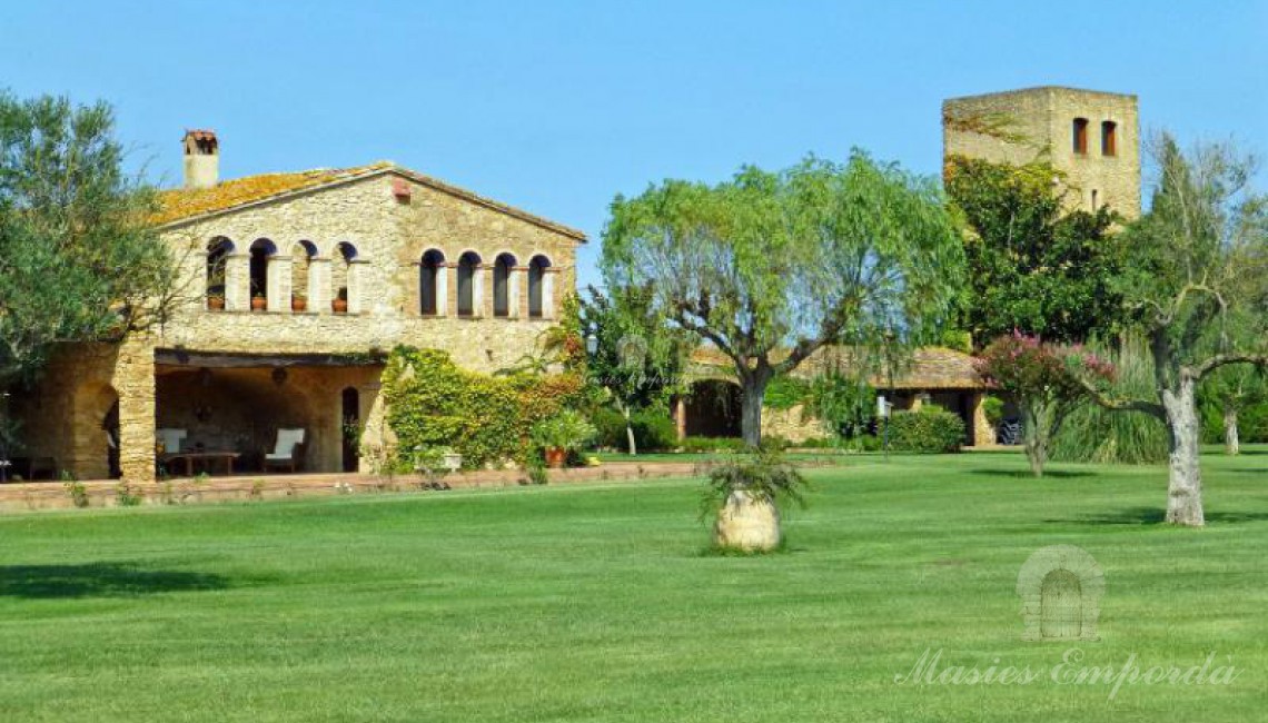 Vista lateral de la masía, los porches anexos y de la torre a ella con el jardín en primer plano.