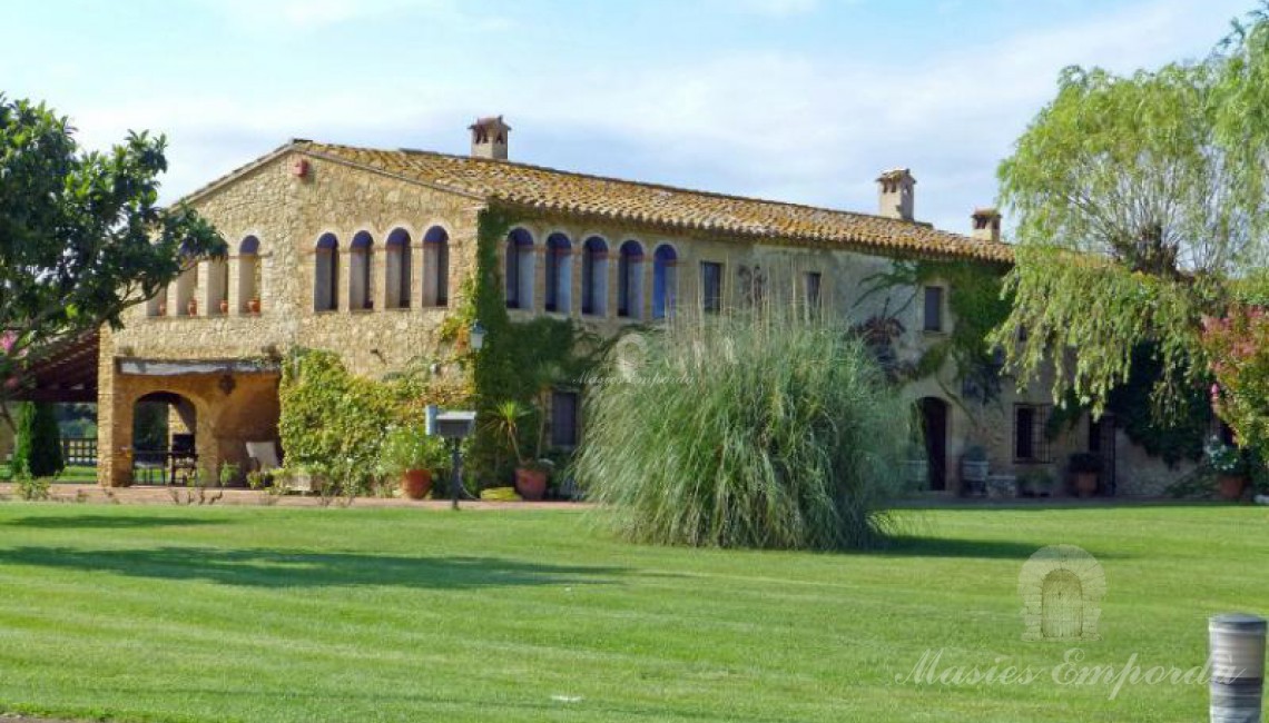 Vista lateral de la masía y los porches anexo a ella rodeada del gran jardín 