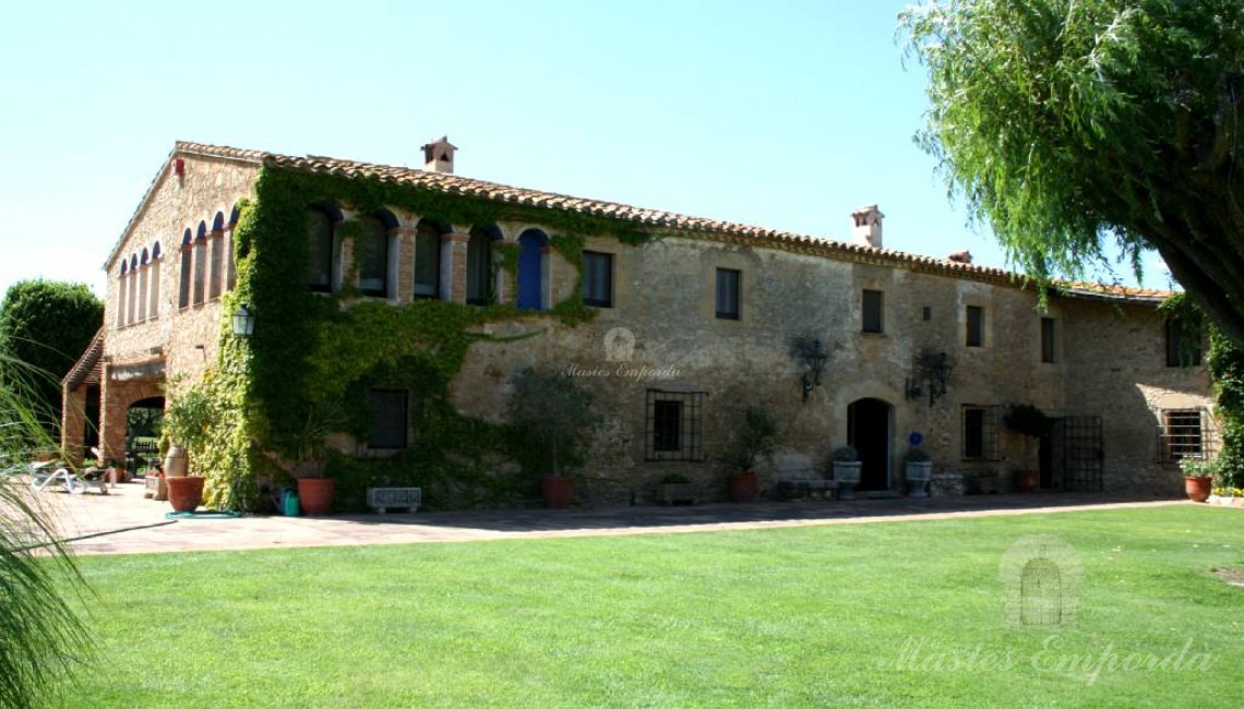 Vista lateral de la masía y los porches anexo a ella rodeada del gran jardín y al fondo la antigua torre de defensa la propiedad que está ubicada Regencos Baix Empordà