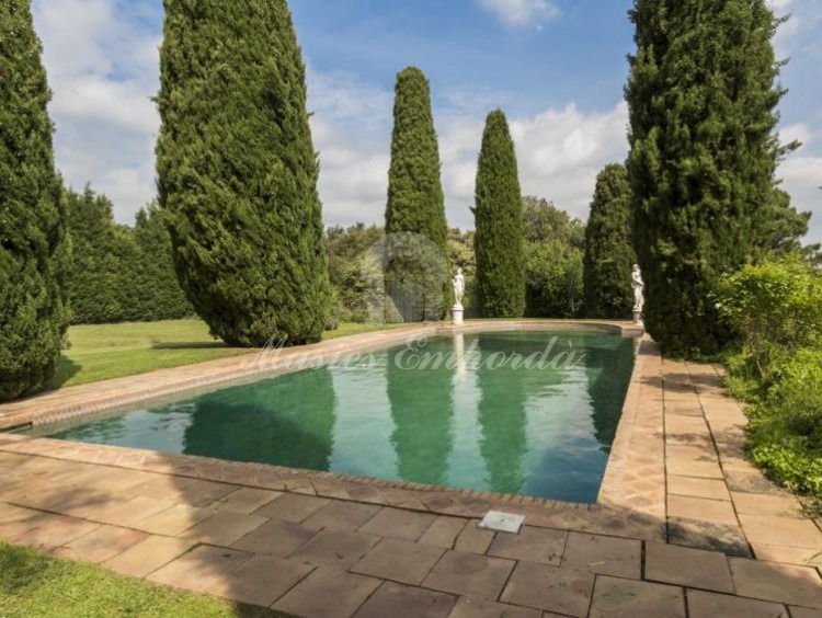 Vista de la piscina de la masía rodeada de cipreses 