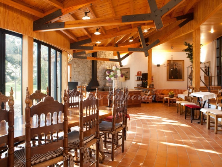 Vista general del gran comedor de la casa de invitados con una gran mesa de madera, el salón con chimenea, con vigas y cubierta de madera